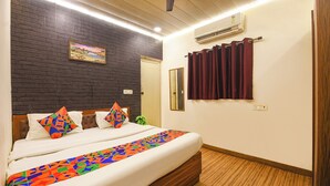 A hotel room with a bed, a dark brick wall, a painting, a mirror, and a window with curtains. - Fabhotel Z Heart (New Delhi)