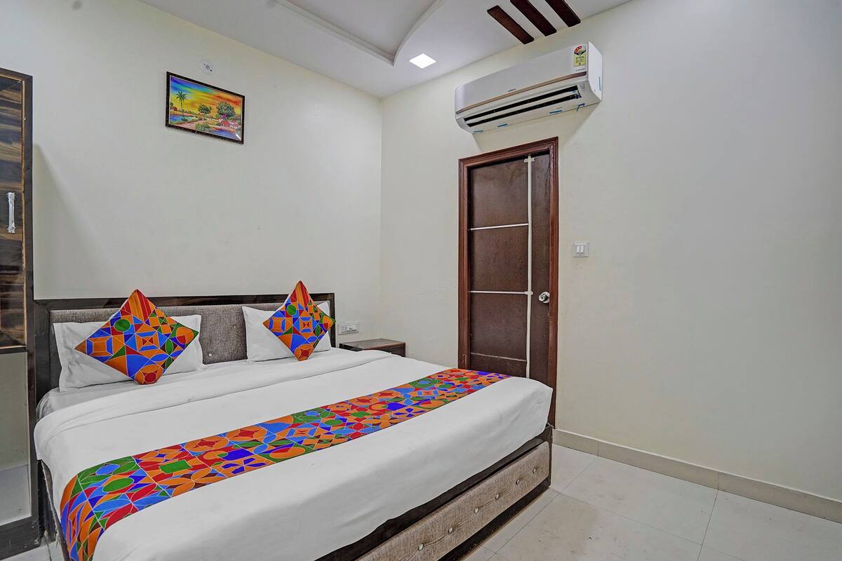 Une chambre à coucher comprenant un lit, des oreillers, une table de chevet, un appareil de climatisation et une porte.