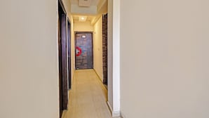 A narrow hallway with a wooden floor, a door with a number plate, and a red circular object on the door. - Fabhotel Stay Inn I (Noida)