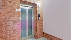 An elevator with a metallic finish and frosted glass doors, set against a textured wall with a wooden pattern. - Fabhotel Stay Inn I (Noida)