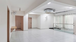 A spacious, well-lit room with white tiled floors, a wooden bench, a door, and a glass railing overlooking a balcony. - FabHotel Srinidhi Stay Inn - HSR Layout (Bangalore)