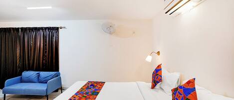 Una habitación de hotel con una cama, un sofá azul, un ventilador de pared y un cojín decorativo.