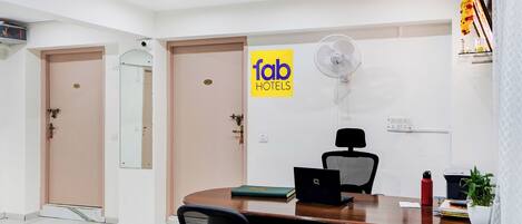 A conference room with a wooden table, black office chairs, a laptop, a desktop computer, a standing fan, and a 'fab hotels' sign on the wall.
