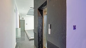 A modern hallway with a glass door, a metal sign, and a tiled floor. - Fabhotel Groom Room (Noida)