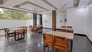 A spacious dining area with multiple tables and chairs, large windows, and ceiling fans. - Fabhotel Groom Room (Noida)