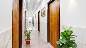 Un pasillo de hotel con puertas de madera, letreros numerados y plantas en macetas.