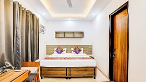 Habitación de hotel con cama de madera, escritorio, silla, ventilador de techo y una puerta.