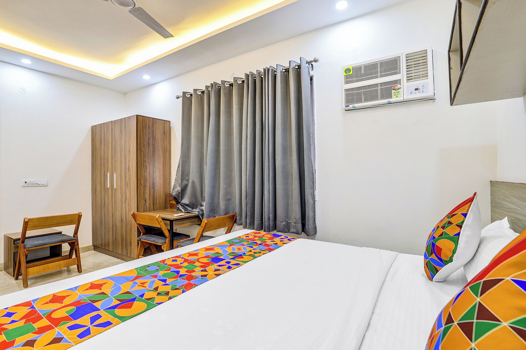Habitación de hotel con cama, escritorio, silla, armario y ventana con cortinas.