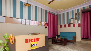 A hotel reception area with a reception desk labeled "DECENT FAB HOTELS," a blue sofa, a small table with a plant, and a fire extinguisher on the wall. - Fabhotel Decent (New Delhi)