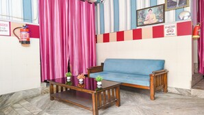 A room with a blue sofa, a glass-top coffee table, and pink curtains. - Fabhotel Decent (New Delhi)