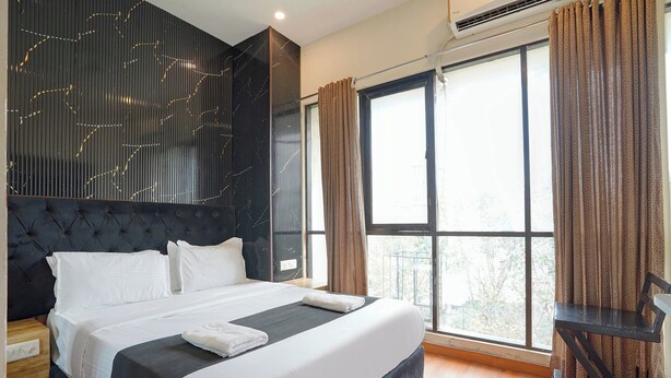 A modern bedroom with a large bed, a headboard with a geometric pattern, a window with curtains, and a small table. - Fabhotel Freedom Star (Mumbai)
