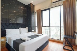 A modern bedroom with a large bed, a headboard with a geometric pattern, a window with curtains, and a small table. - Fabhotel Freedom Star (Mumbai)