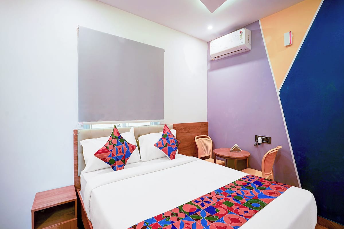 A hotel room with a bed, a small table, a chair, and an air conditioning unit.
