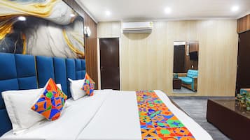 A modern hotel room with a large bed, a blue headboard, a colorful geometric bedspread, and a large abstract painting on the wall.