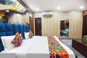 A modern hotel room with a large bed, a blue headboard, a colorful geometric bedspread, and a large abstract painting on the wall. - Fabhotel Happy Residency (New Delhi)