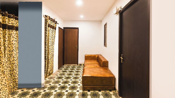 A hallway with a patterned floor, a wooden door, a bench, and a blue wall. - Fabhotel South Paradise (New Delhi)