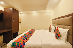 A hotel room with a bed, a wooden wardrobe, and a headboard. - Fabhotel South Paradise (New Delhi)