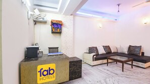 A hotel reception area with a reception desk labeled 'fab hotels', a sofa set, a small table, and a wall-mounted air conditioning unit. - Fabhotel South Paradise (New Delhi)