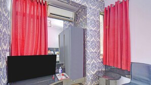Habitación con una amplia televisión de pantalla plana, un espejo, una pequeña mesa con una botella de agua y una silla.