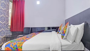 Una habitación de hotel con una cama, cabecera, ventana con cortinas rojas y pared con diseño.