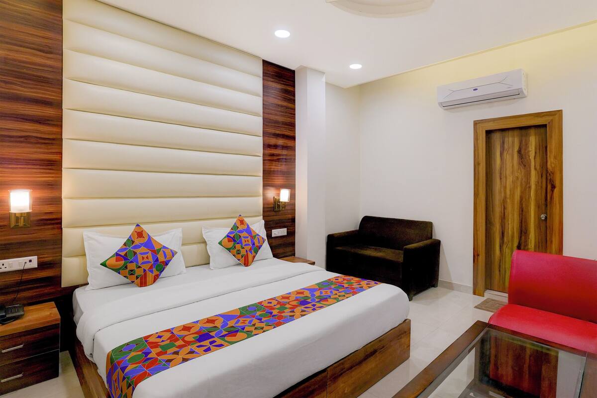 A hotel room with a large bed, a wooden headboard, a red chair, and a wooden door.