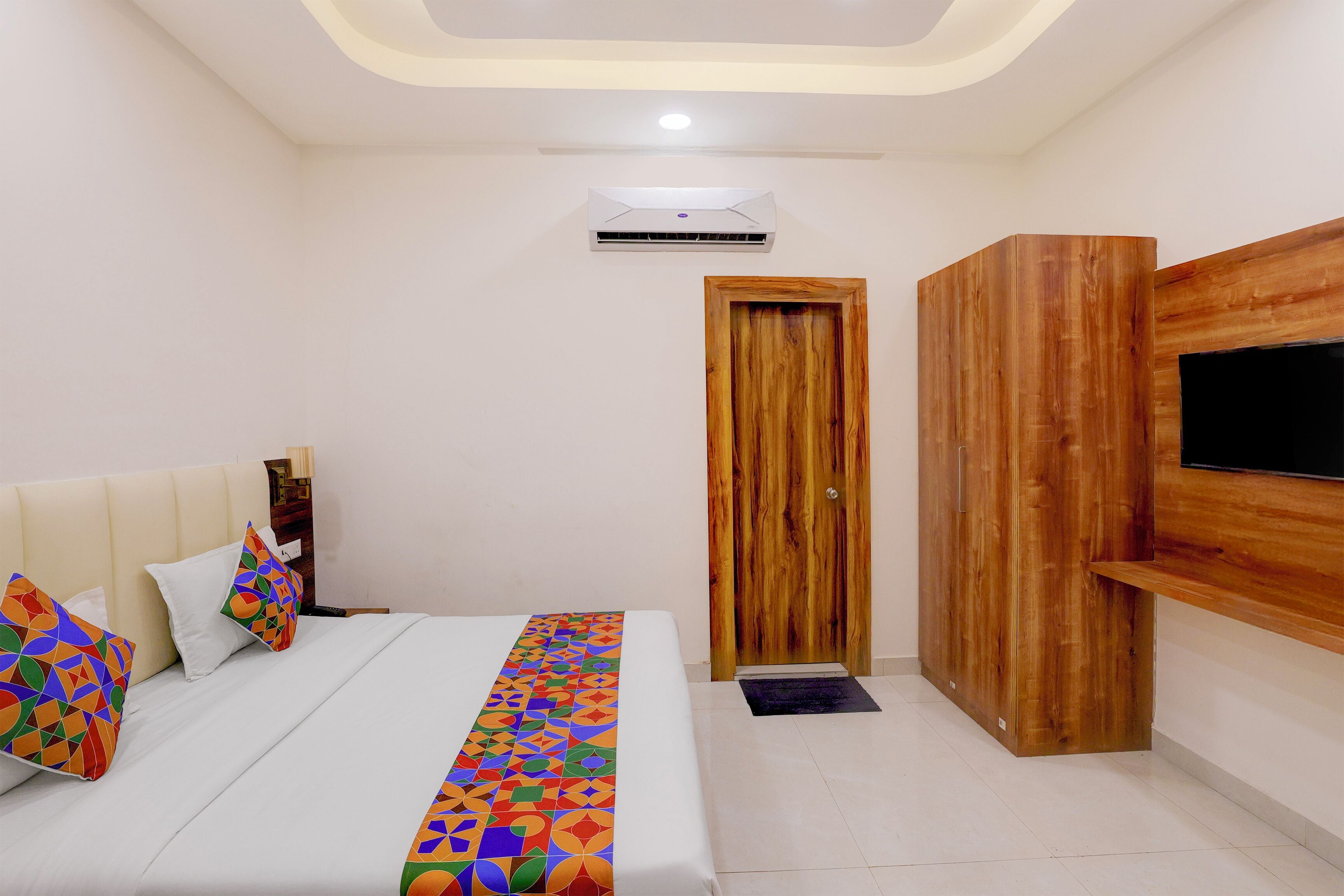 A bedroom with a bed, pillows, a TV, an air conditioner, and a wooden door.