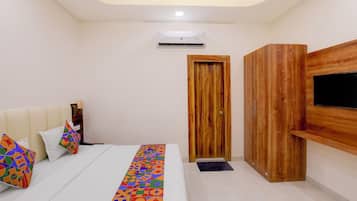 A bedroom with a bed, pillows, a TV, an air conditioner, and a wooden door.