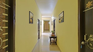 A hallway with yellow walls, framed pictures, a small table with a plant, and a door with a key lock. - FabHotel Rush Inn (Hyderabad)