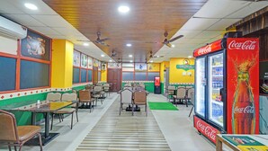 A restaurant with tables and chairs, a Coca-Cola refrigerator, and a ceiling fan. - FabHotel Rush Inn (Hyderabad)