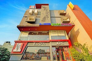 Un edificio de varios pisos con un restaurante KFC en la planta baja, un letrero de Fab Hotels arriba y un salón de belleza Green Trends en un piso superior.