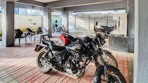 Un espace extérieur abrité, doté d’un sol carrelé, où sont stationnées plusieurs motos, ainsi que quelques chaises et tables.