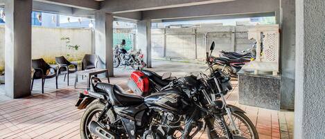 A covered outdoor area with tiled flooring, several motorcycles parked, and a few chairs and tables.