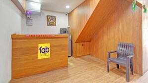Un espace d’accueil avec un comptoir en bois portant l’inscription « fab hotels », un ventilateur de plafond et un mur en bois avec un plafond en pente.