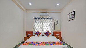 Une chambre d’hôtel comprenant un lit, une table de chevet, une commode, un miroir et un climatiseur fixé au mur.