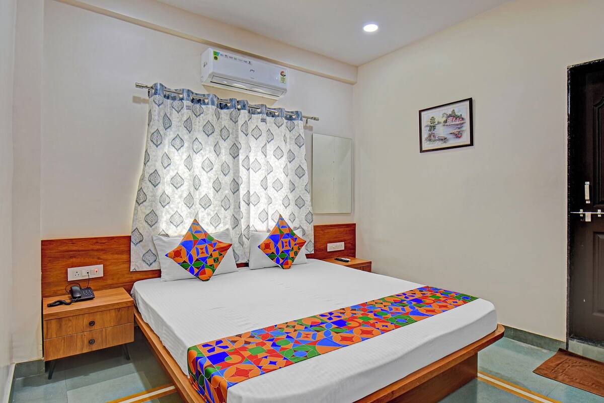 A hotel room with a bed, a bedside table with a phone, a nightstand, a wall-mounted air conditioner, and a door.