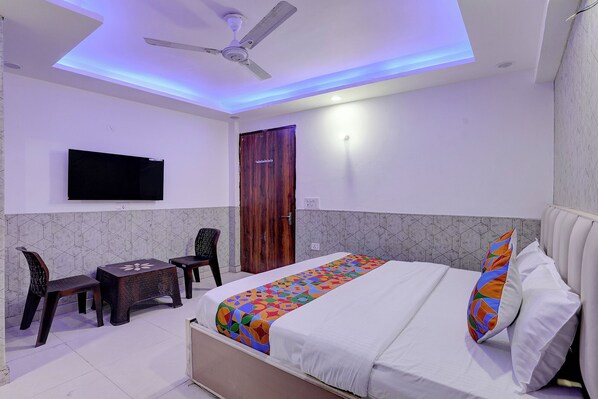 A hotel room with a bed, a desk, a chair, a television, and a ceiling fan. - Fabhotel Akki Residency (Noida)