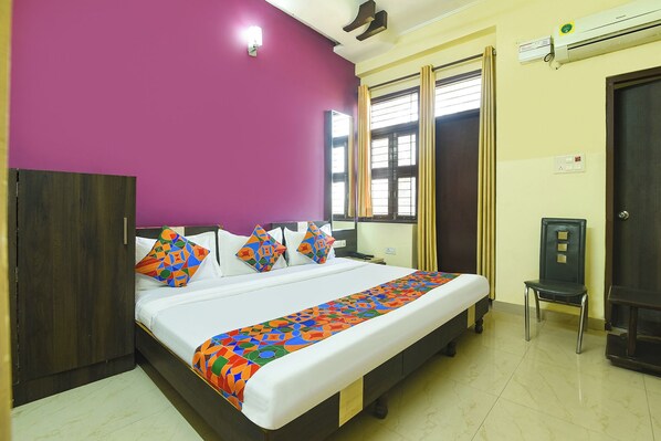 A hotel room with a bed, a chair, a window with curtains, an air conditioning unit, and a wall-mounted light. - Fabhotel Highway Pride (Jaipur)