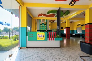 Una reception hotel con un cartello 'fab hotels', una parete di vetro con un cartello 'WELCOME' e vista su una zona verde all'esterno.