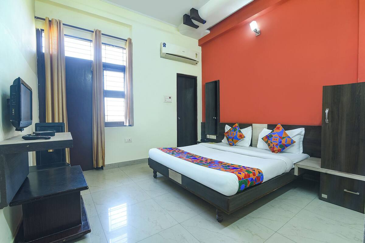 A hotel room with a bed, a desk with a television, and a window with curtains.