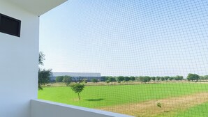 Una habitación con un ventanal grande que da a un campo verde con algunos árboles y un edificio lejano.