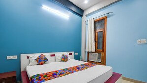 A bedroom with a bed, a nightstand, a window with curtains, and a wall socket. - Fabhotel Sunshine Inn (Lucknow)