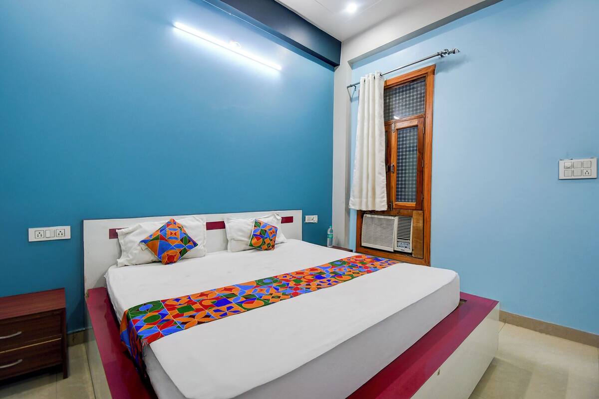 A bedroom with a bed, a nightstand, a window with curtains, and a wall socket.