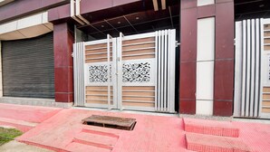 A building entrance with a closed metal gate featuring decorative patterns, a red tiled pathway leading to the entrance, and a wooden bench outside. - Fabhotel Sunshine Inn (Lucknow)