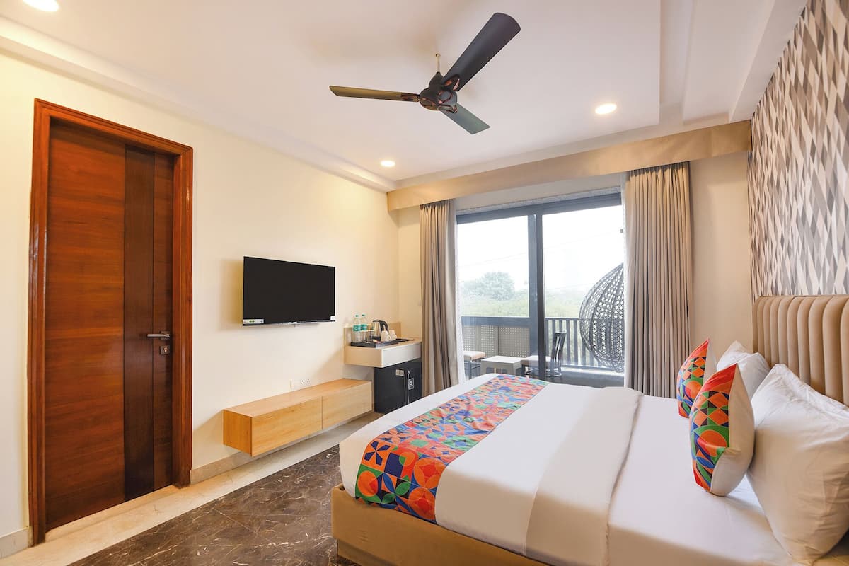 A hotel room with a bed, a TV, a ceiling fan, a window with curtains, and a balcony with a chair.