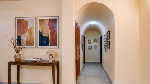 Un pasillo con una consola de madera, dos cuadros abstractos, un jarrón con ramas y una puerta que da a otra habitación.