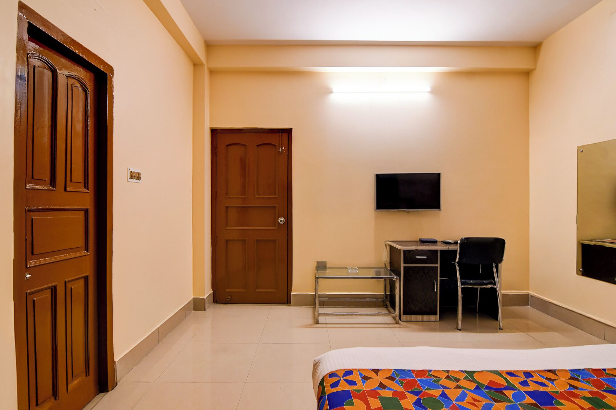 A hotel room with a bed, a desk with a chair, a television, and a door.