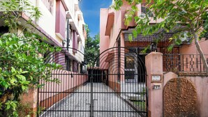 Una entrada porticada a una zona residencial con un camino pavimentado que conduce a un acceso vehicular con portón.