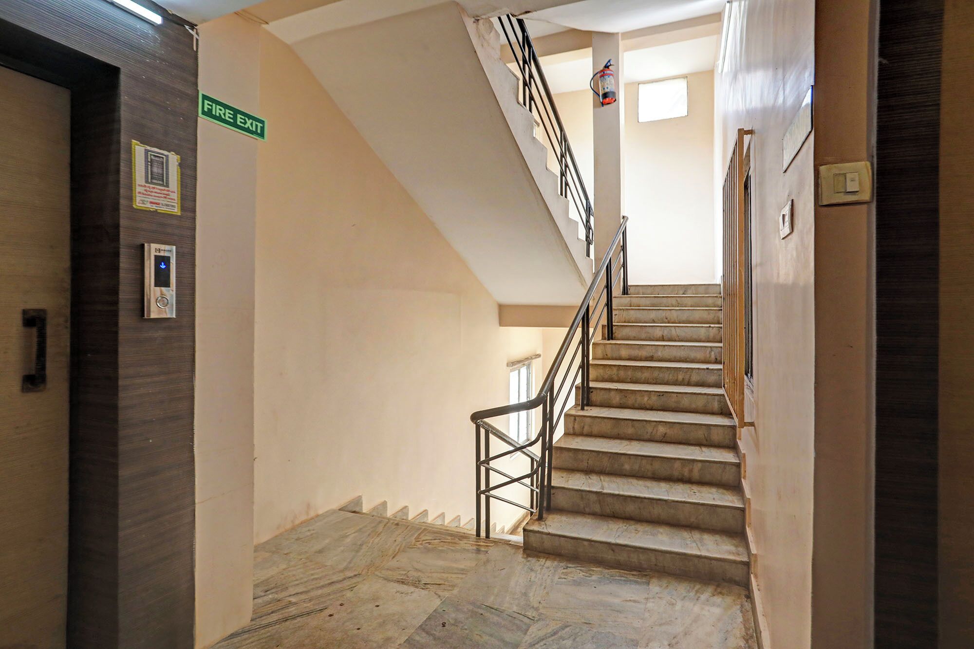 A staircase with a metal railing, a fire exit sign, and a fire extinguisher on the wall.