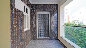 Un couloir étroit avec un mur à motifs noirs et oranges, une porte ornée de motifs géométriques et une fenêtre donnant sur un espace vert.