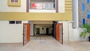 L’entrée d’un bâtiment, avec deux portails ouverts, une enseigne au-dessus indiquant « RS Grand Inn », et un pot de fleurs placé à droite.